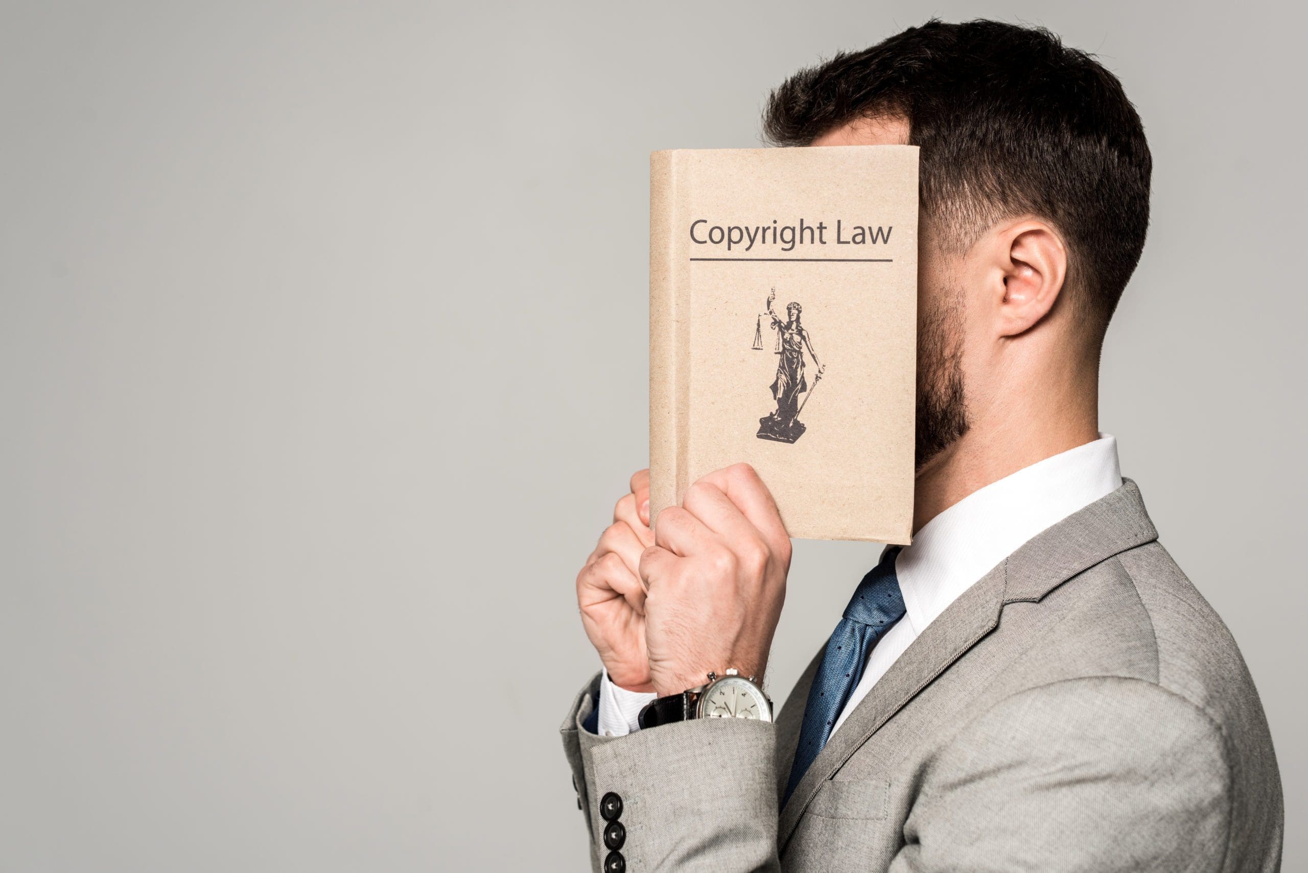 side view of lawyer obscuring face with copyright law book isolated on grey